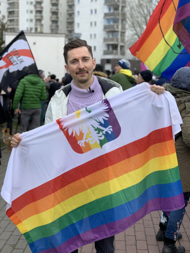Martin Kmiecik holding a rainbow-coloured flag of Poland